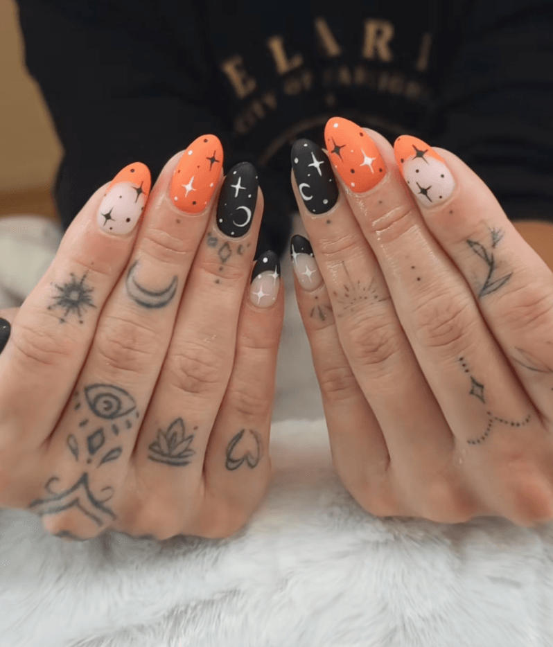 Matte black and orange nails with crescent moons.