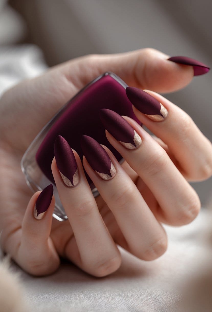 A close-up of a hand with medium-length burgundy nails featuring matte accents.