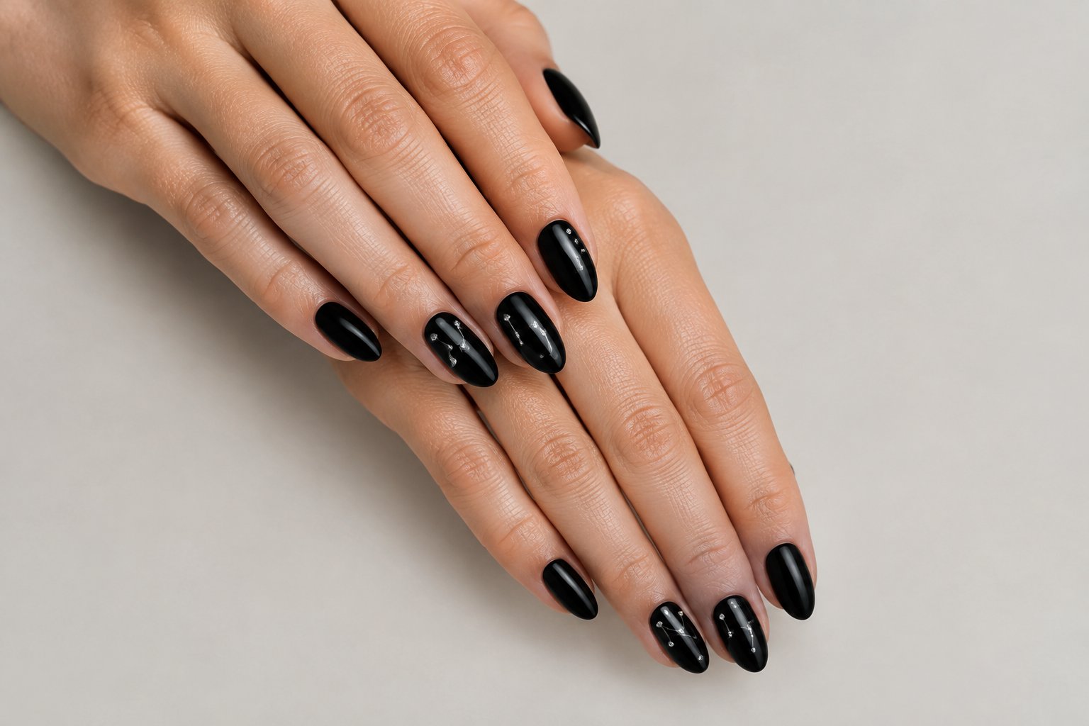Hands with glossy black nails decorated with tiny rhinestone constellations.