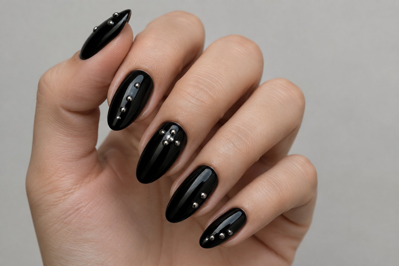 A hand with glossy black nails decorated with small silver studs.