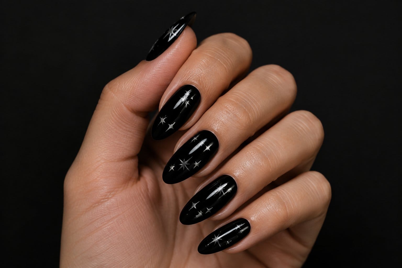 A hand with glossy black nails decorated with silver stars.