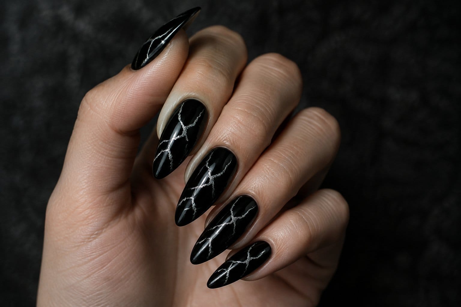 A hand with black nails decorated with silver lightning-crack designs.
